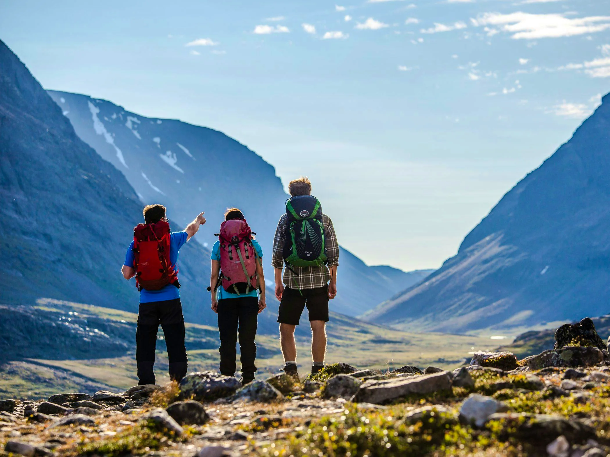 Hikers on a guided tour look out over a valley surrounded by high mountain peaks in clear weather.