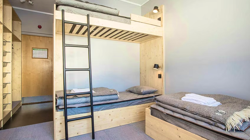 Bright hostel-style room with wooden bunk beds and neatly made single beds.