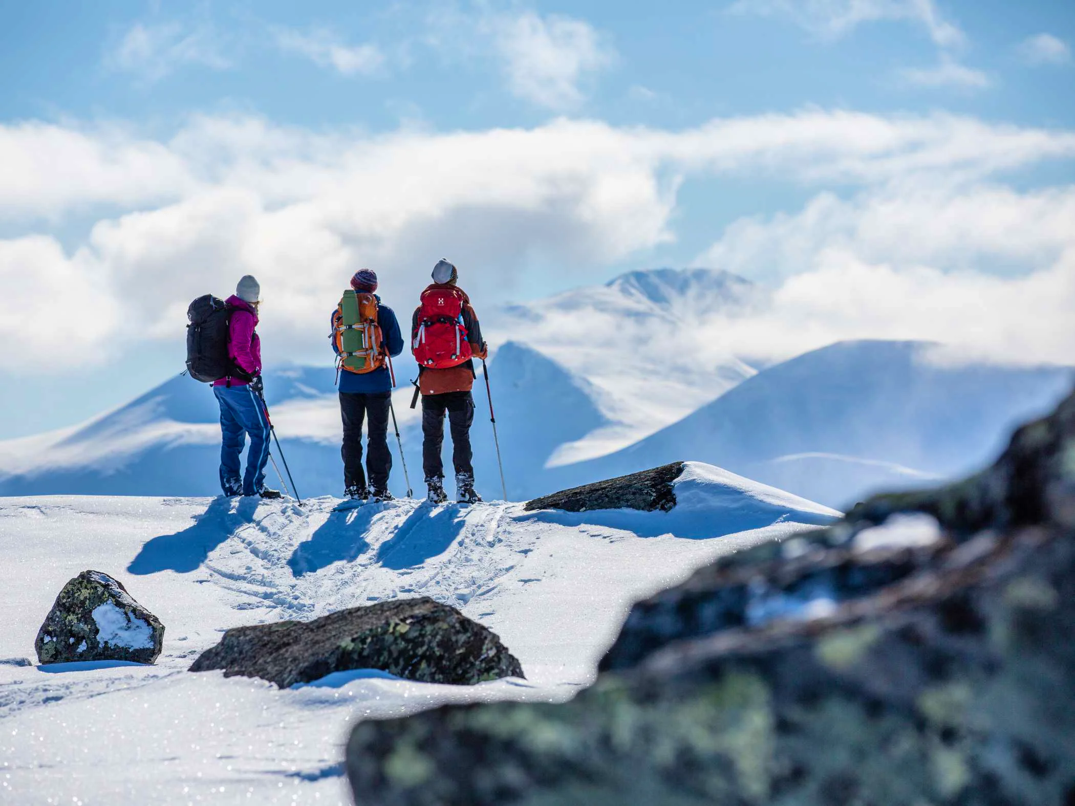 Three skiers are standing on a mountain looking at the mountain view.