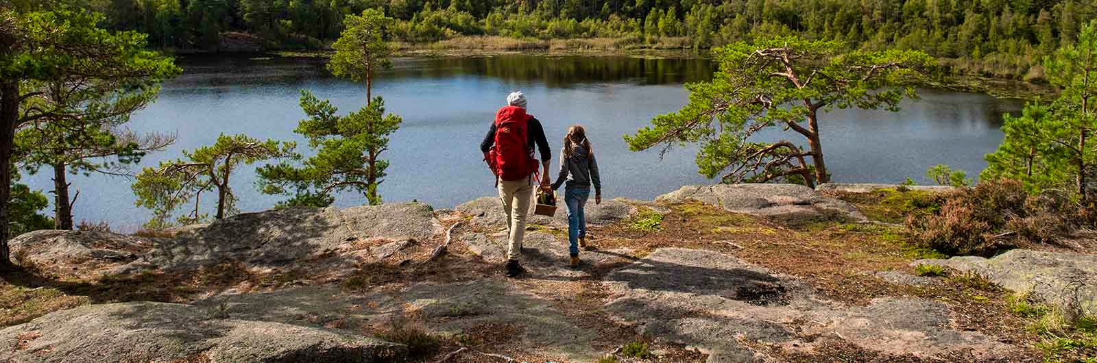 A father and his daughter hiking to a view point over a lake in the forest.