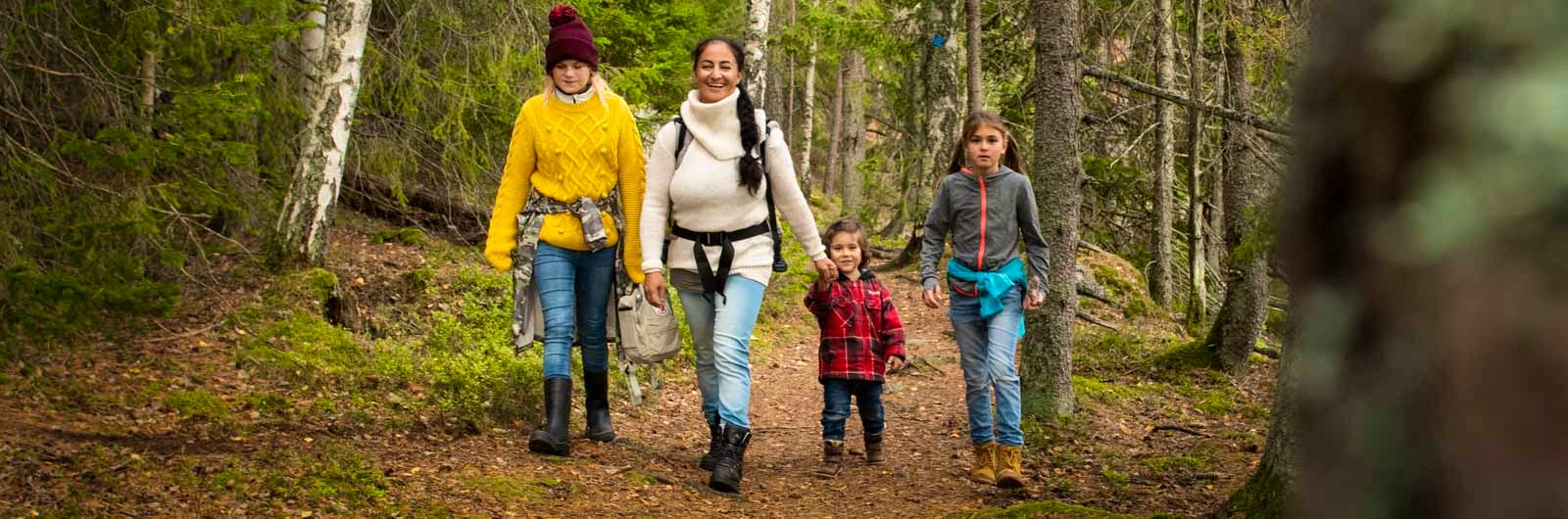 Two adults and two kids walking on a trail in the forest.