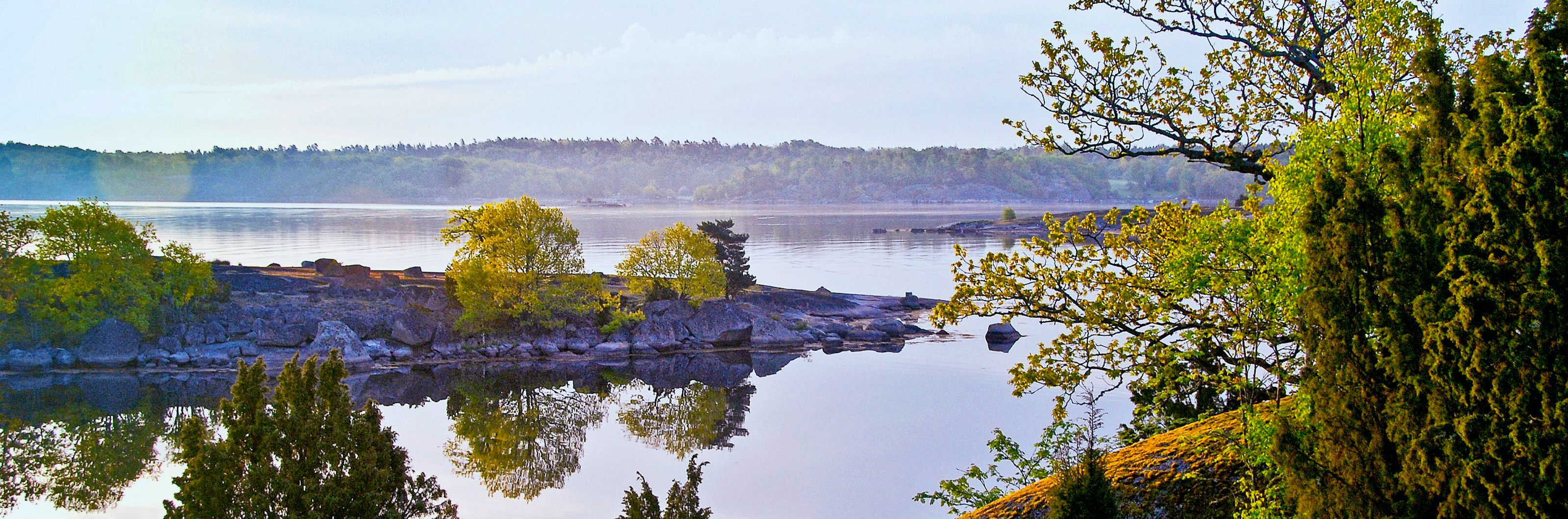 Peaceful morning scenery in the Stockholm archipelago with rocky islands, green trees, and mirror-like reflections on the water.
