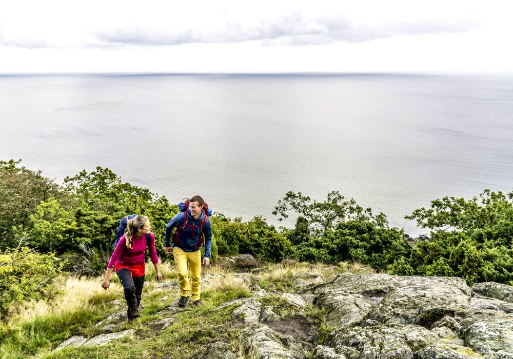 Two people hiking up a hill on a trail by the sea. 