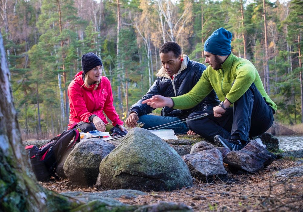 Three people light up a fire in the forest.