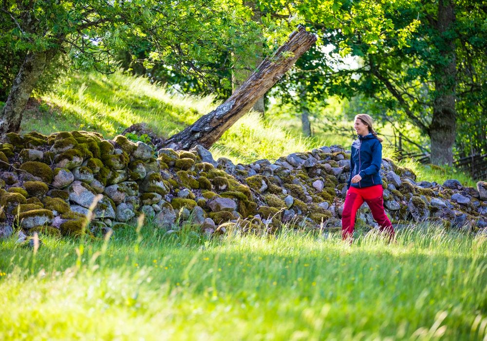 A female hiker hiking along a stonewall in the forest.