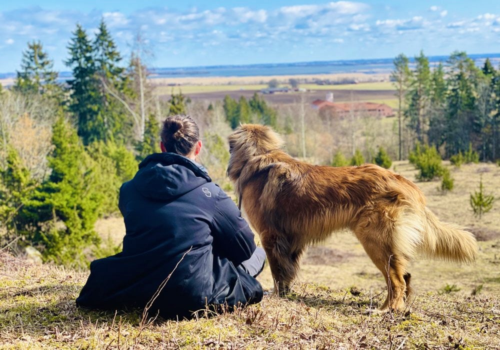 A lady sitting on a hill with his dog.