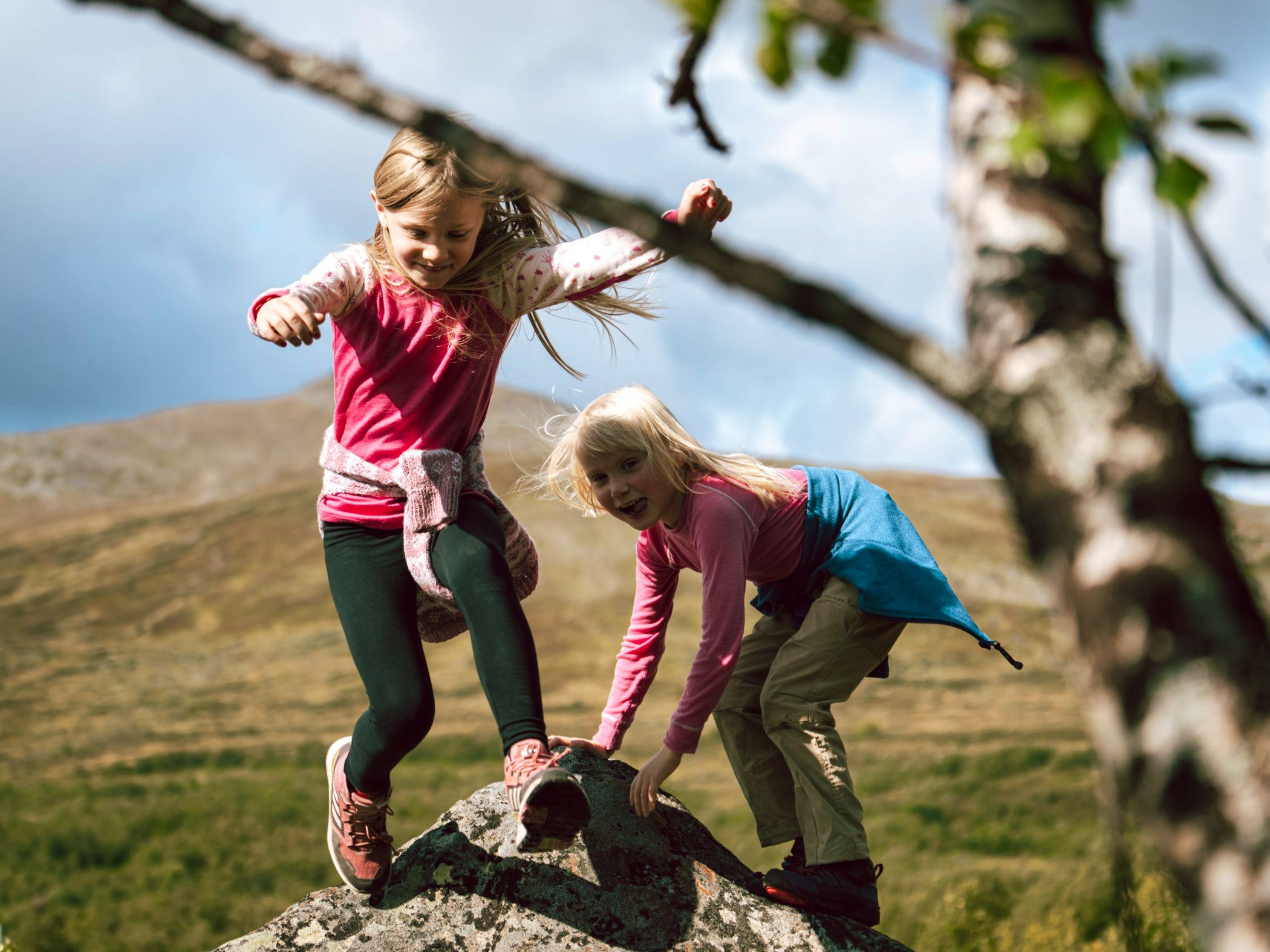 Two kids playing on a rock in the mountains. 