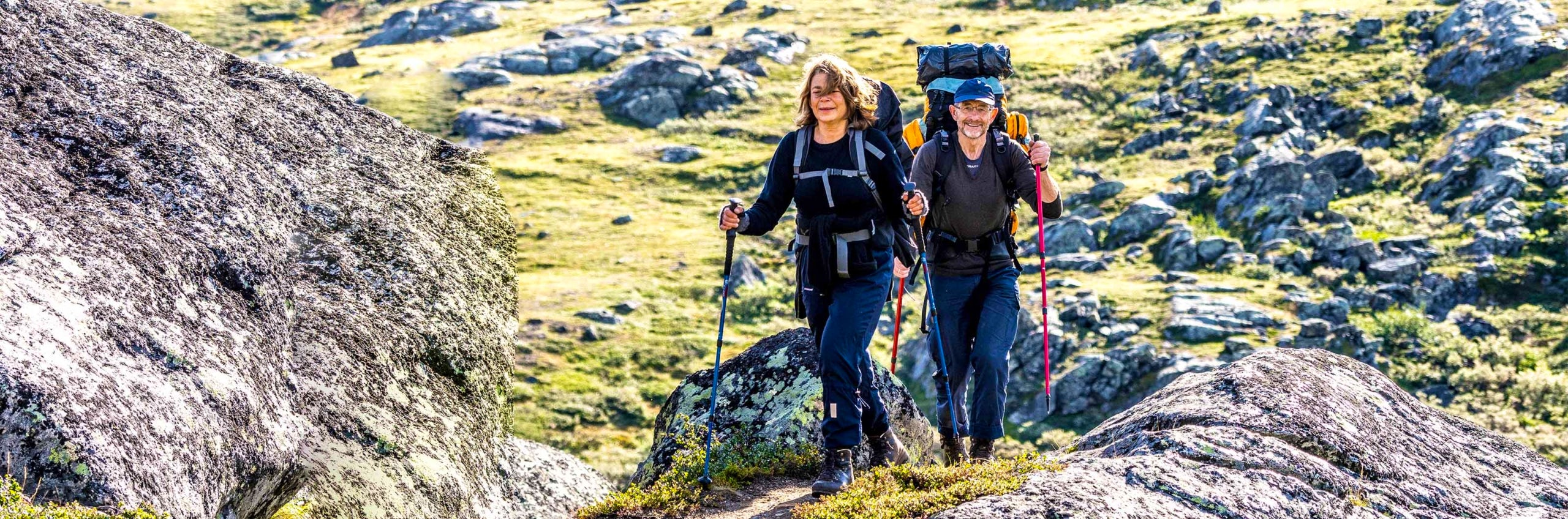 A couple is walking in the mountains with trekking poles.