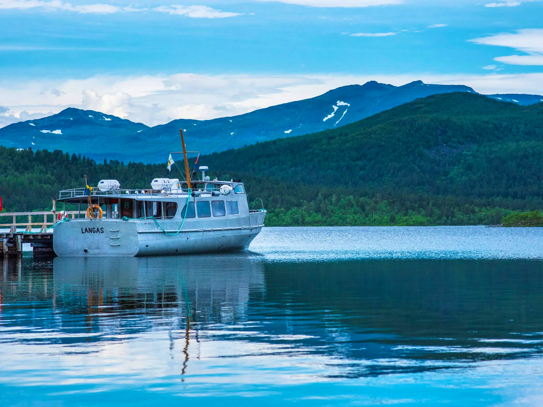Boat by a dock with mountains and forest in the background.
