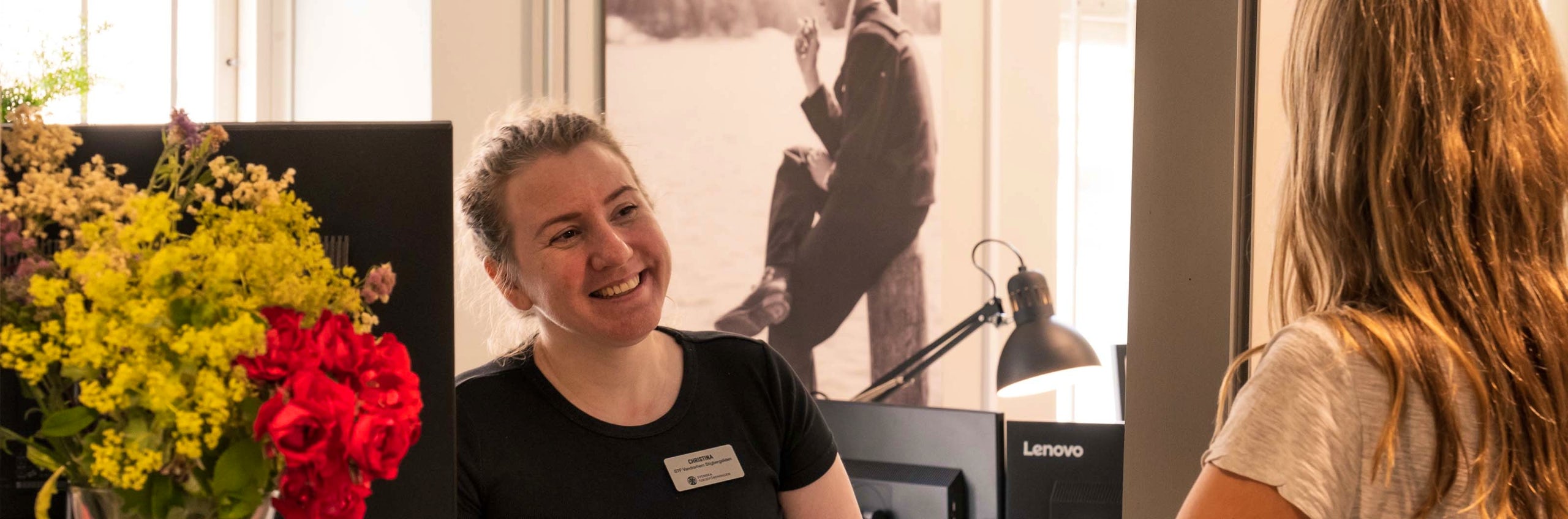 A receptionist smiles and welcomes a guest at check-in.