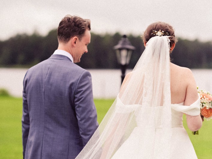 A newlywed couple walking hand in hand down towards the water.