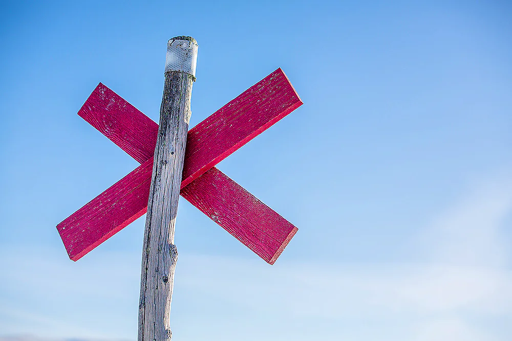 Red trail marker cross on a pole in a snowy mountain landscape guiding the winter trail.