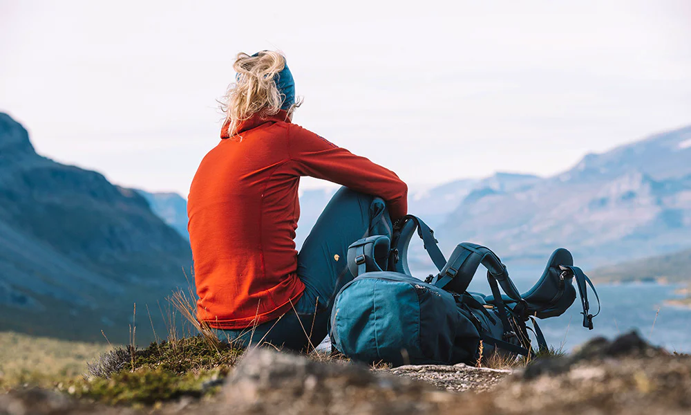 Person sitting on a hillside next to a backpack overlooking a mountain valley.