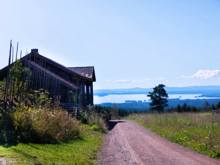 A wooden house and a dirt road with views over Siljan.