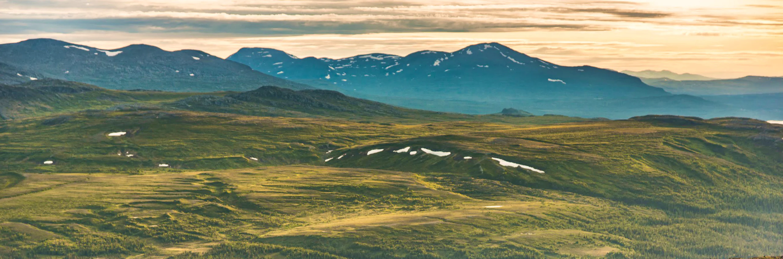 Mountain landscape at sunset with rolling hills and distant peaks.