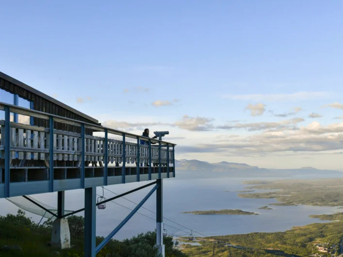 A person standing on the balcony of Aurora Sky Station overlooking a lake.