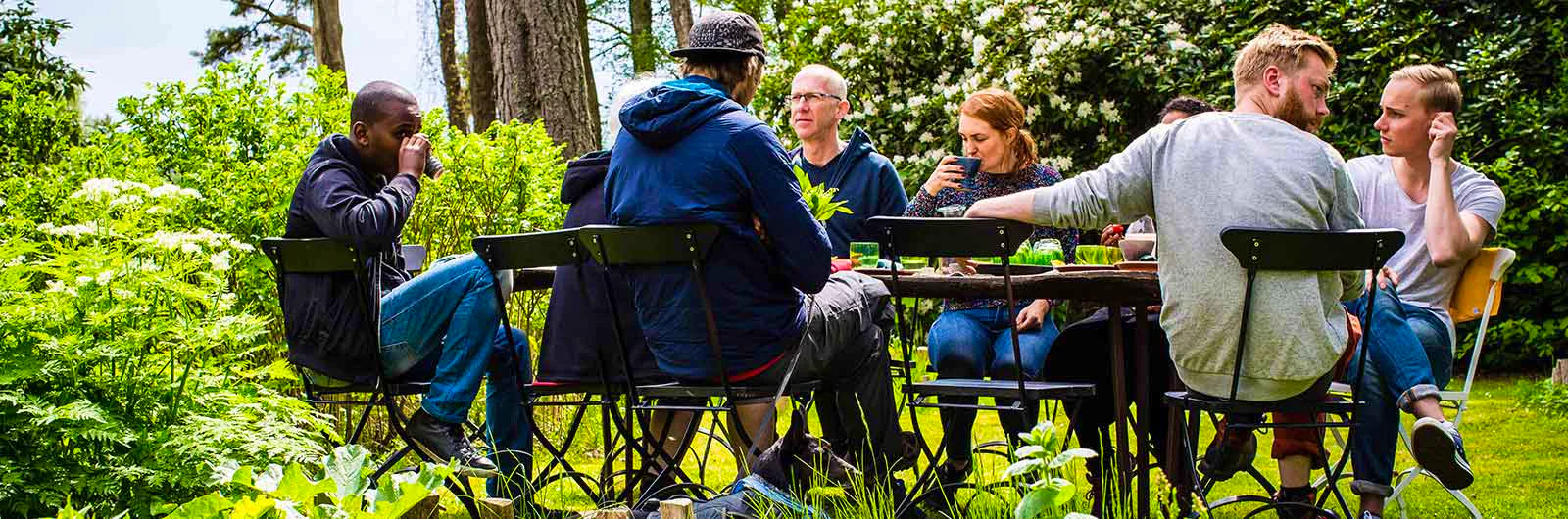 Group of people sitting outdoors having a meal in a garden setting.