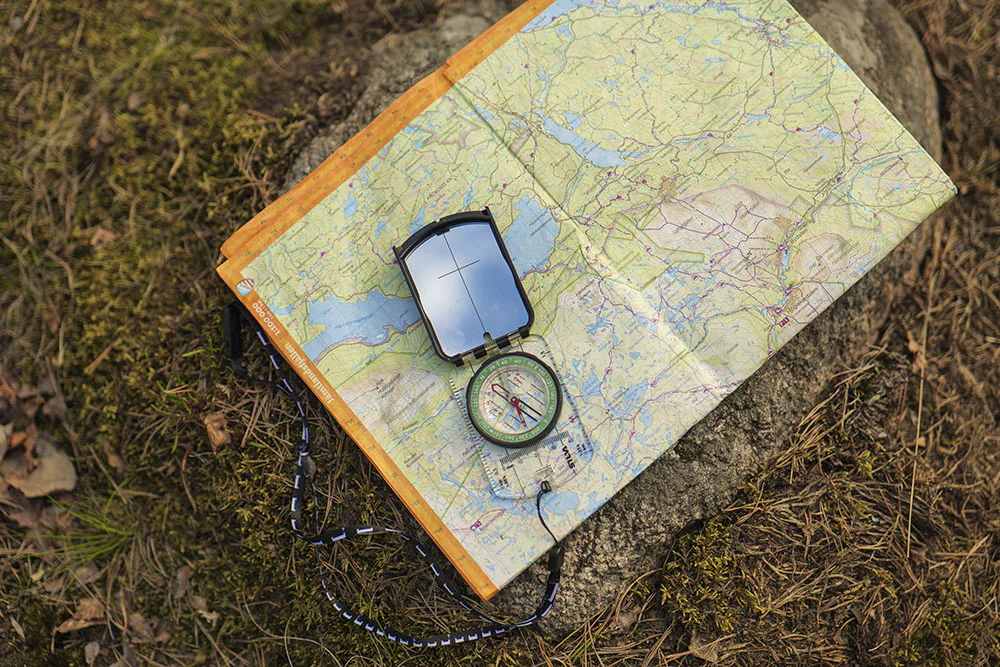 Map and compass placed on the ground for navigation outdoors.