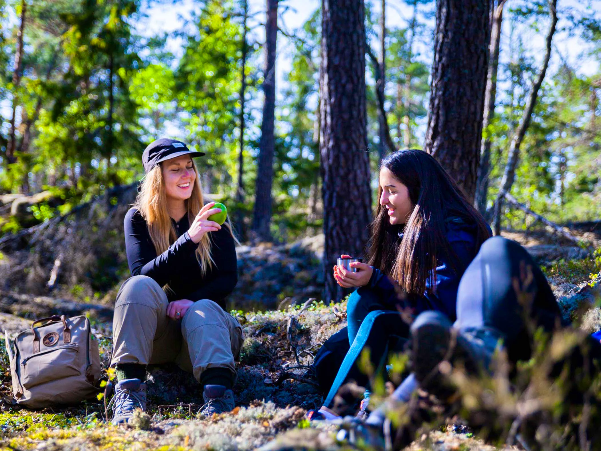 Two people sitting in a forest, taking a break with coffee and fruit.