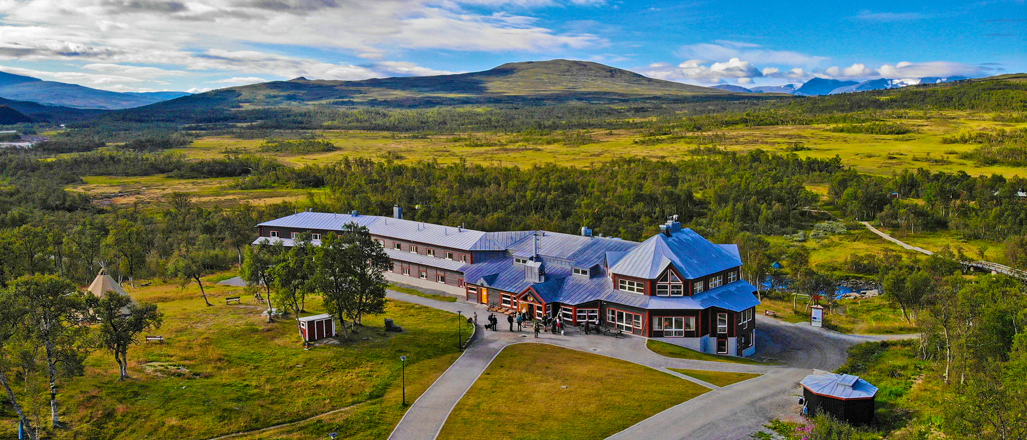 Mountain station building seen from above, surrounded by forest and open landscape.