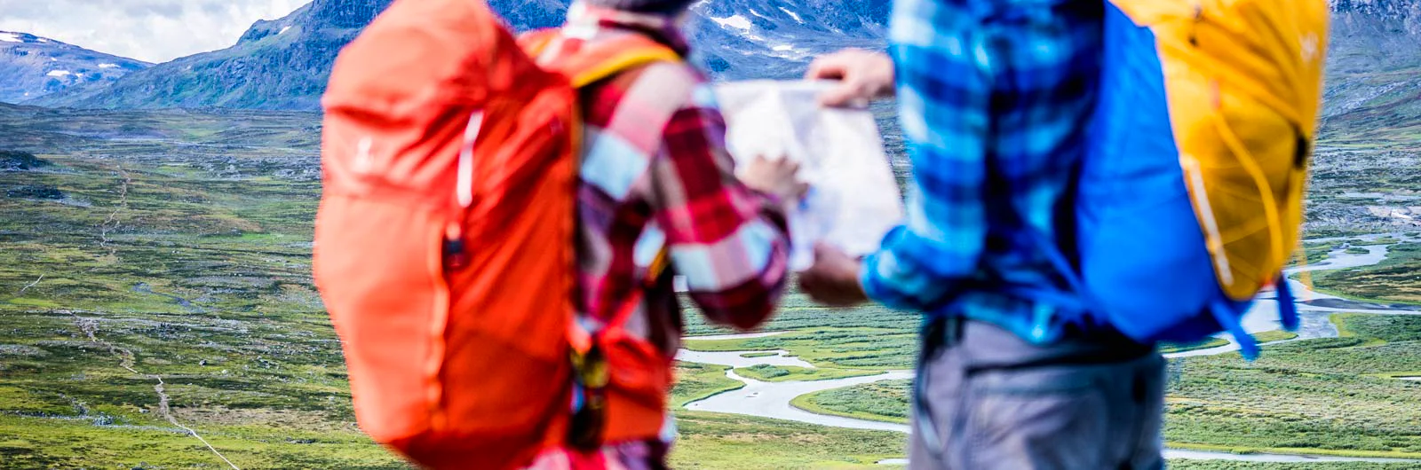 Two hikers with backpacks looking at a map in a mountain landscape.