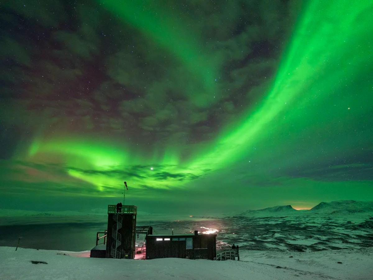 Aurora Sky Station in Abisko beneath vivid northern lights above the snow-covered mountain landscape.