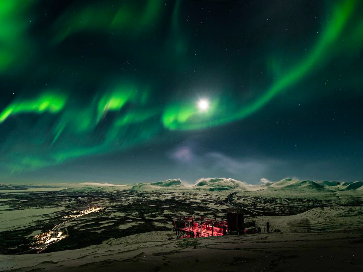 Northern lights and moonlight above the snow-covered mountain landscape at Aurora Sky Station in Abisko.