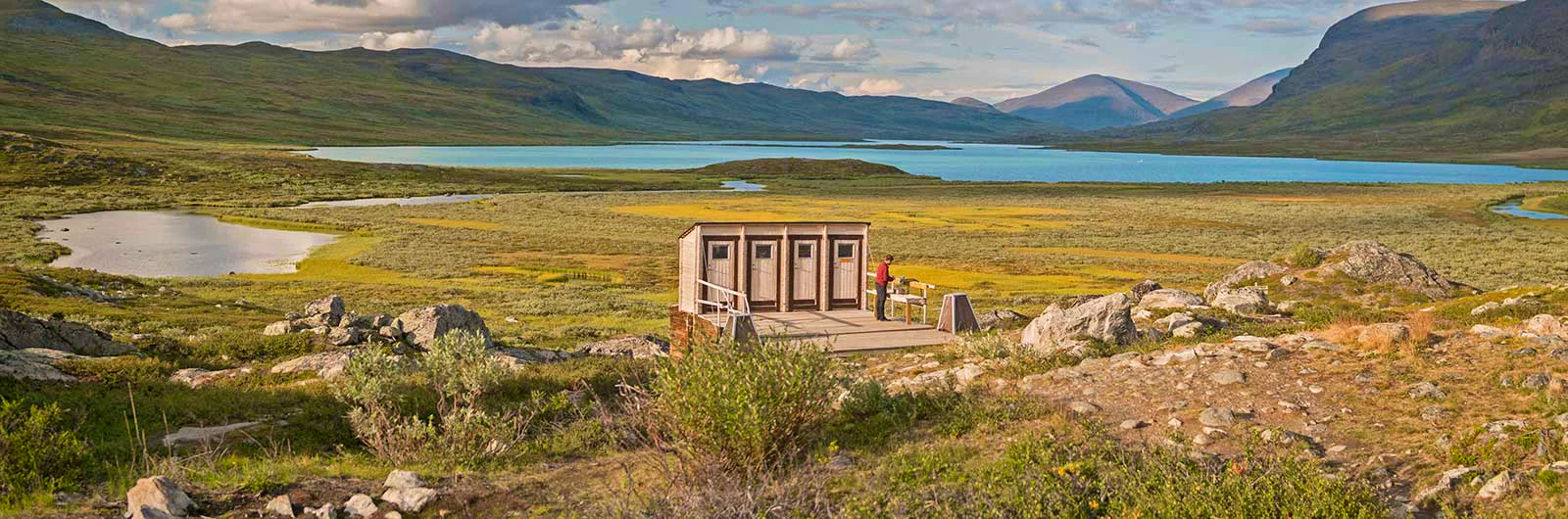 Four outdoor toilets at STF Alesjaure mountain cabin, overlooking a lake and mountains.
