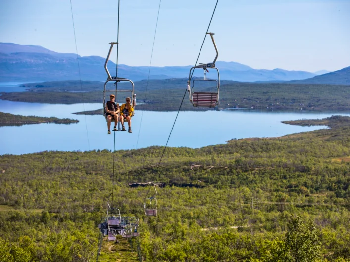 Two people ride a ski lift over a lake.